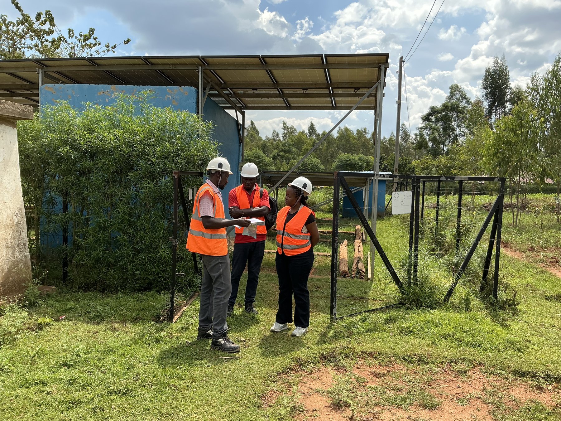 Eliane Nirere and site staff in hard hats and safety vests beside a solar minigrid